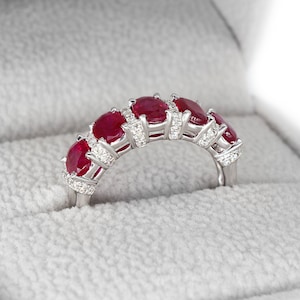 May include: A ring featuring a row of red rubies and small diamonds set in white metal.