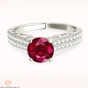May include: A silver ring with a large red ruby gemstone surrounded by a double row of smaller diamonds.
