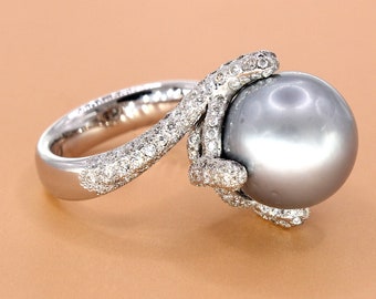 Pode incluir: Um anel de prata com uma grande pérola cinza engastada em um design de garra com diamantes.