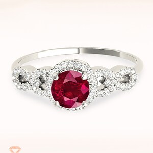 May include: A silver ring featuring a red ruby gemstone set in a halo of smaller diamonds. The band has a delicate, interwoven design.
