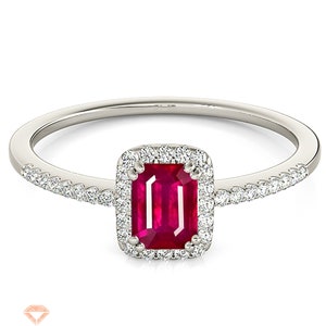 Könnte beinhalten: Ein silberner Ring mit einem roten Smaragdschliff-Edelstein, der von einem Heiligenschein aus kleineren Diamanten umgeben ist. Die Ringschiene ist ebenfalls mit kleineren Diamanten besetzt.