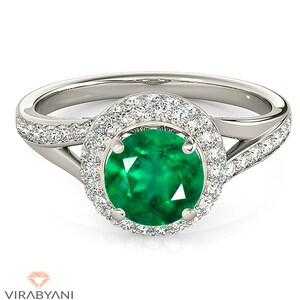 Könnte beinhalten: Ein silberner Ring mit einem großen Smaragd, der von einem Halo aus kleineren Diamanten umgeben ist. Die Ringschiene ist verdreht und mit zusätzlichen Diamanten besetzt.