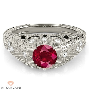 May include: A vintage-style engagement ring featuring a large, round, red ruby gemstone surrounded by smaller, round, white diamonds. The ring has a delicate, filigree design and is set in white gold.