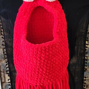May include: A handmade red plush bag with white crocheted eyes and yellow antennae. The bag has a large opening and a fringe at the bottom. The bag is displayed on a black surface.