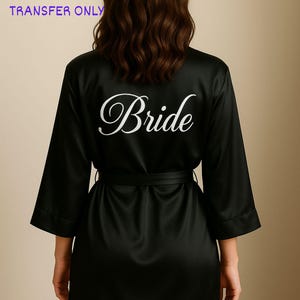 Peut inclure: Robe en satin noir avec le mot "Bride" en écriture blanche sur le dos. La robe a des manches larges et une ceinture assortie. Le texte en haut indique "HTV, IRON ON TRANSFER ONLY".