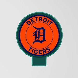 May include: A Detroit Tigers logo in a circular design. The logo features the team name and a stylized "D" in navy blue on an orange background, framed by a green border. The design is on a green rectangular base.