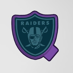 May include: A shield-shaped graphic with a purple border and a teal interior. The word "RAIDERS" is at the top. Below is a helmeted face with crossed swords. A purple "Q" shape extends from the bottom.