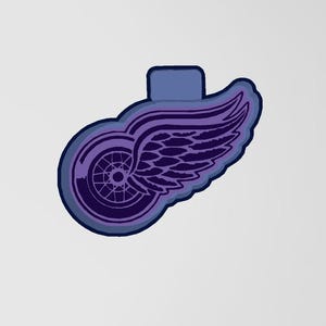 Könnte beinhalten: Stilisiertes Logo mit einem lilafarbenen geflügelten Rad-Design, blauem Umriss und blauem rechteckigem Oberteil. Das Emblem ist auf weißem Hintergrund.