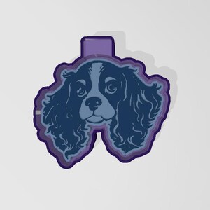 May include: A blue and white Cavalier King Charles Spaniel dog head design with a purple border and a purple rectangle at the top. The dog's face is detailed with eyes, nose, and fur.
