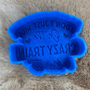 May include: Blue silicone mold with the text "I don't just ride on the crazy train, I drive it" in white.