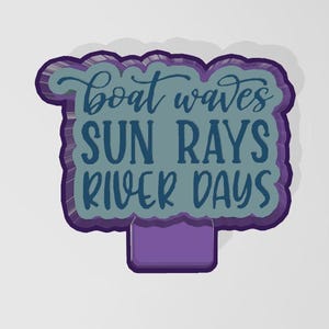 Puede incluir: Un letrero decorativo con las palabras "boat waves SUN RAYS RIVER DAYS" en color turquesa. Tiene un borde y una base morados, ideal para la decoración de verano. La fuente es juguetona.