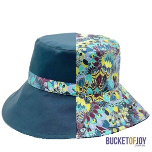 Puede incluir: Un sombrero de cubo azul verdoso con un estampado floral colorido en un lado. El sombrero tiene un ala ancha y una corona plana.