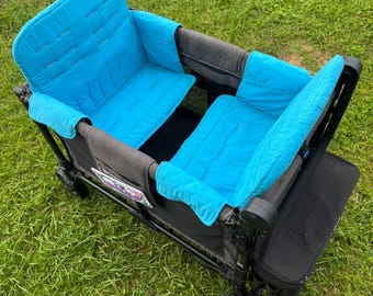 May include: A black and gray double stroller wagon with two turquoise padded seats. The wagon has black wheels and is sitting on a grassy lawn. The seats have a quilted design.