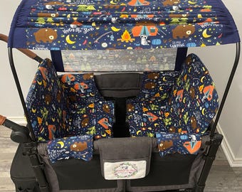 May include: A navy blue wagon with a canopy and interior fabric featuring a camping theme with bears, tents, and stars. The canopy has the text "Under the Stars" and "Let's Go Camping". The wagon has a gray interior and black frame.