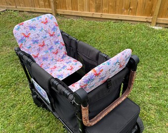 May include: A black utility wagon with a butterfly-patterned seat and backrest. The seat fabric features colorful butterflies on a light purple background. The wagon has a brown handle and is on a grassy lawn.