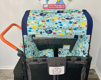 May include: A black and gray wagon with an orange handle and a canopy featuring a sea life pattern. The canopy and interior are decorated with colorful fish, turtles, and anchors. The wagon has black wheels and storage pockets.