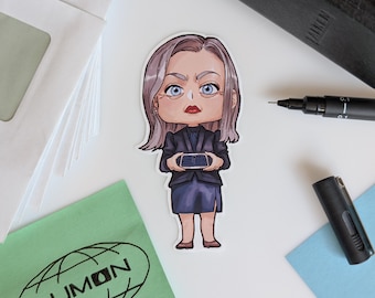 May include: A sticker depicting a cartoon character in a dark blue suit, holding a small keyboard. The character has grey hair, blue eyes, and red lips. The sticker is on a white surface with a green cloth printed with the word "LUMON".