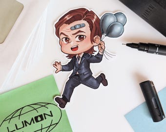May include: A cartoon sticker of a man in a suit running and holding three grey balloons. The man has brown hair, a bandage on his forehead, and a tie. The sticker is on a white surface with a green envelope that has the word "LUMON" printed on it.
