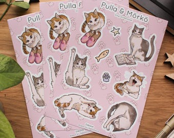 May include: A sheet of pink vinyl stickers featuring illustrations of cats in various poses. The stickers are part of a sheet titled "Pulla & Mörkö" and include a cat reading a book, a cat with a fish, and a cat with a paw print.