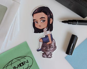 May include: A sticker showing a cartoon illustration of a person in a school uniform seated on the head of an older person. The sticker is on a white surface with a black pen, pen cap, and a green cloth with the word "LUMON".