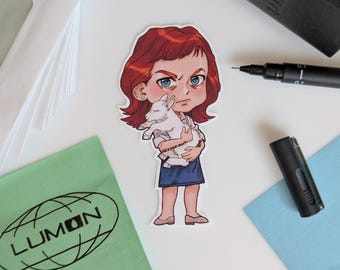 May include: A sticker depicting a cartoon character with red hair and blue eyes, clutching a white lamb. The character wears a blue skirt and has an intense expression. The sticker is on a white surface, alongside other items.