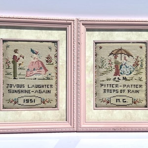 May include: Two framed needlepoint artworks with pink frames. One reads "Joyous Laughter Sunshine-Again 1951" and depicts a person with a flower. The other reads "Pitter-Patter Drops of Rain M.C." and shows a couple under an umbrella. Both have floral accents.