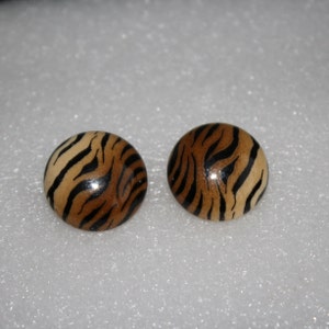 Puede incluir: Dos pendientes redondos de madera con un diseño de rayas de tigre. Los pendientes tienen una base marrón claro con rayas marrones oscuras. Los pendientes son circulares y tienen un acabado brillante.