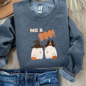 Könnte beinhalten: Ein dunkelblauer Pullover mit dem Text "Me & Boo!" und zwei Cartoon-Geistern, die einen Hexenhut und einen Piratenhut tragen. Die Geister halten orangefarbene Eimer mit Süßigkeiten.