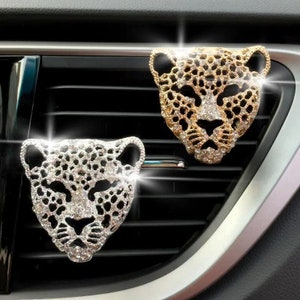 May include: Two car air freshener charms in the shape of a leopard's head. One is silver with clear rhinestones and the other is gold with gold rhinestones.