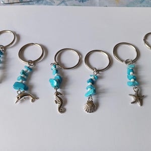 May include: Keyrings with silver rings and turquoise and white beads. Each keyring features a different ocean-themed charm, including an octopus, dolphin, seahorse, seashell, starfish, and turtle. Ideal for those who love the seaside.
