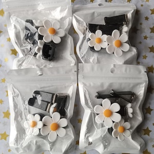 May include: Four clear plastic bags each containing a set of black hair clips and white daisy-shaped hair clips with yellow centres.