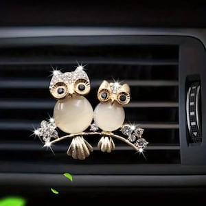 May include: Two gold owl car air freshener charms with white crystal accents and rhinestones. The owls are perched on a branch with rhinestones.