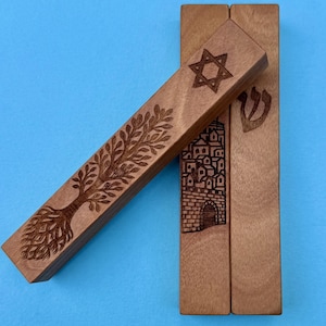 Puede incluir: Carcasa de mezuzá de madera con diseños grabados. Una carcasa presenta una Estrella de David, otra un árbol de la vida y una tercera representa un edificio. Las carcasas son de madera marrón claro sobre un fondo azul.