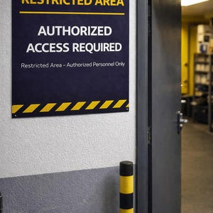 May include: A sign with the words "RESTRICTED AREA AUTHORIZED ACCESS REQUIRED" in white and yellow lettering on a dark blue background. The sign is mounted on a white and gray wall near an open gray door.