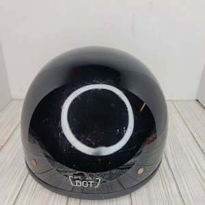 May include: A glossy black motorcycle helmet with a rounded shape. The helmet has a DOT sticker at the bottom and a few small scratches. The helmet has a reflective surface.