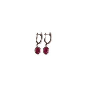 May include: A pair of silver hoop earrings with a dangling red gemstone. The hoops are set with small clear stones.
