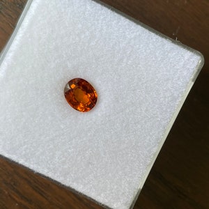 May include: A close-up of a round, orange gemstone on a white background.