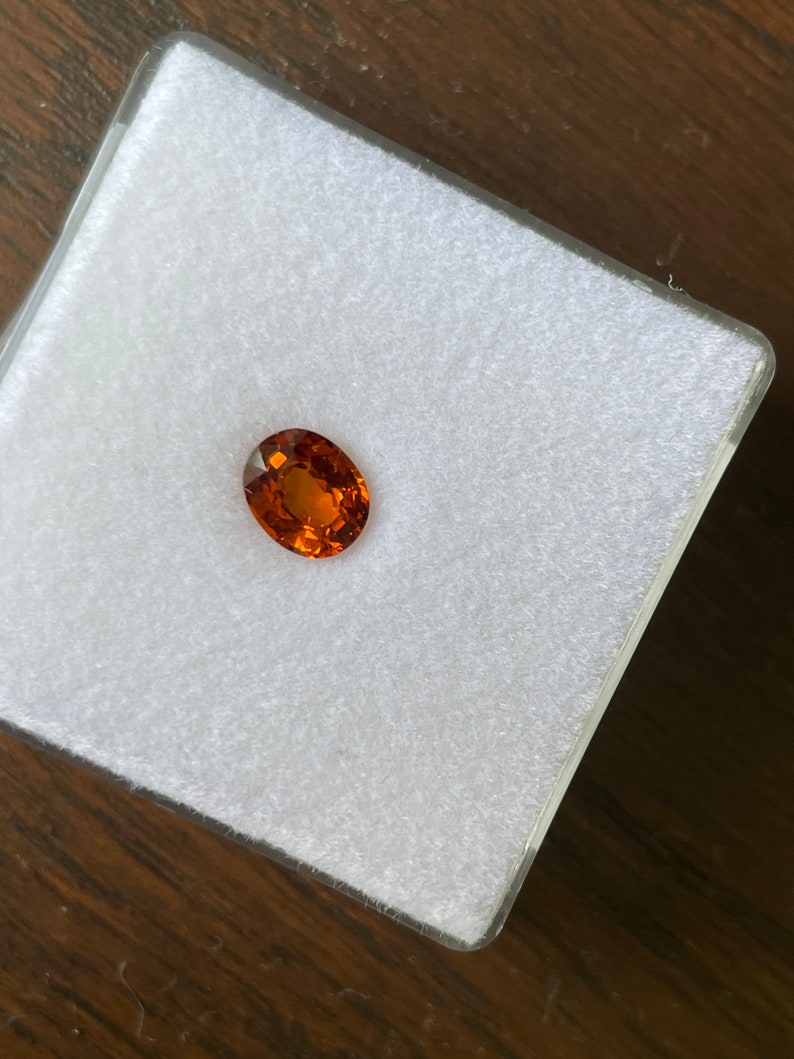 May include: A close-up of a round, orange gemstone on a white background.