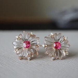 May include: A pair of earrings featuring a pink gemstone set in a carved flower design with clear crystals.