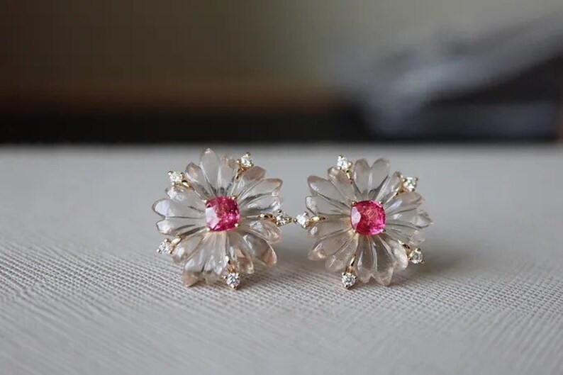 May include: A pair of earrings featuring a pink gemstone set in a carved flower design with clear crystals.