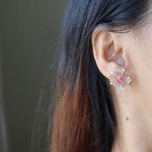 May include: A pair of flower-shaped earrings with a pink center stone and clear crystals.