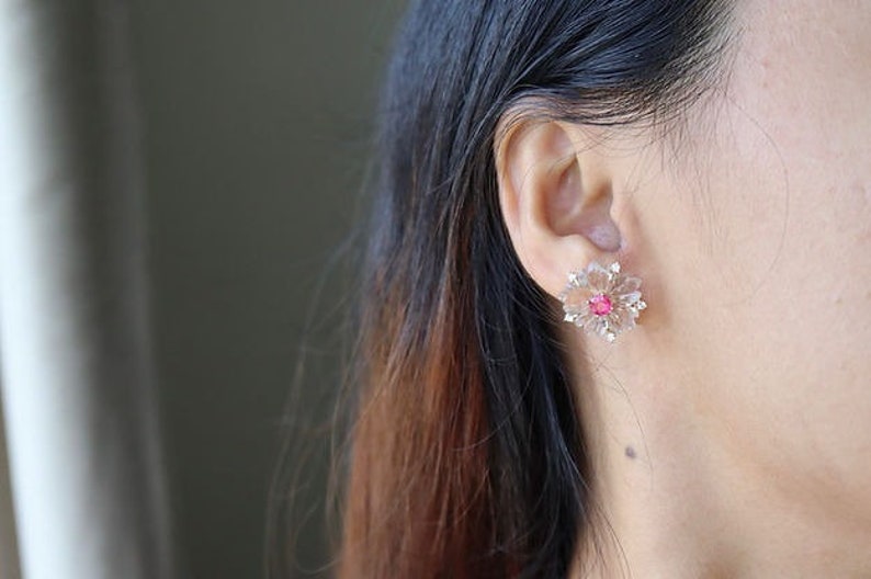 May include: A pair of flower-shaped earrings with a pink center stone and clear crystals.
