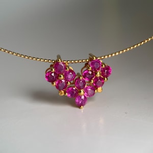 Puede incluir: Un collar de oro con un colgante compuesto por tres grupos en forma de flor de piedras preciosas redondas de color rosa vibrante. El colgante cuelga de una delicada cadena de oro con textura de cuentas, creando una pieza de joyería detallada.