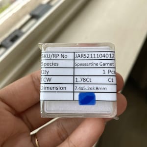 May include: A white label with black text listing the details of a 1.78 carat Spessartine Garnet gemstone. The label includes the SKU/RP number, species, quantity, total carat weight (TCW), and dimensions. The gemstone is 7.4 mm x 5.2 mm x 3.8 mm.