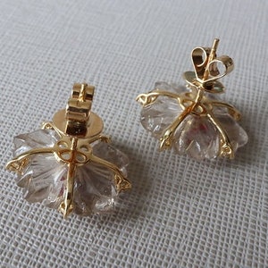 May include: A pair of gold earrings with clear quartz crystals in a flower shape.