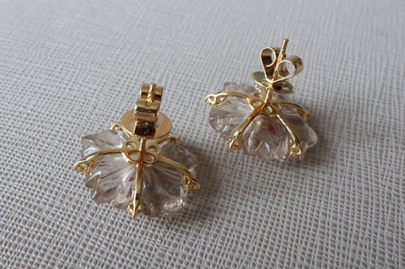 May include: A pair of gold earrings with clear quartz crystals in a flower shape.