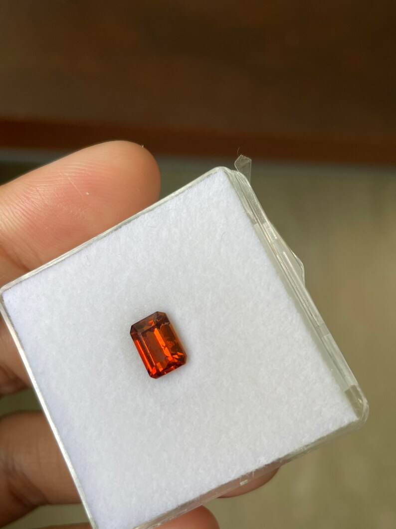 May include: A rectangular, orange gemstone in a white, square, plastic box.
