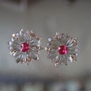 May include: A pair of earrings featuring a clear flower-shaped design with a pink gemstone in the center of each flower.