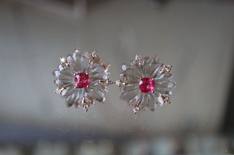 May include: A pair of earrings featuring a clear flower-shaped design with a pink gemstone in the center of each flower.