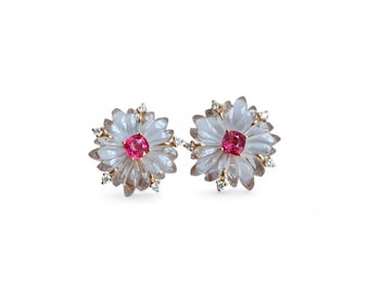 Puede incluir: Un par de pendientes de oro con diseño de flor. Cada pendiente tiene una piedra preciosa rosa en el centro rodeada de piedras transparentes.